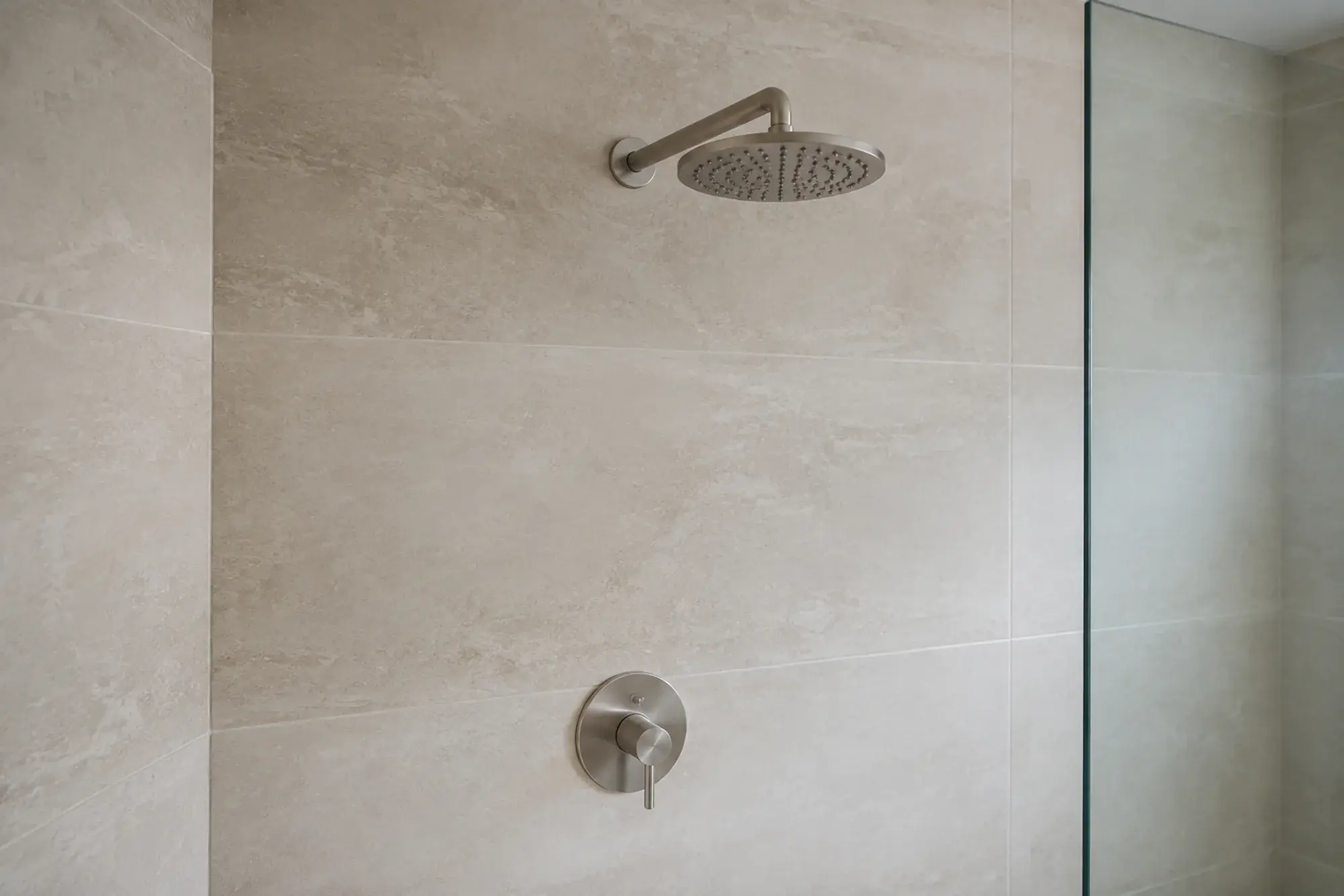 Shower concept with brushed nickel trim against pale stone tile.